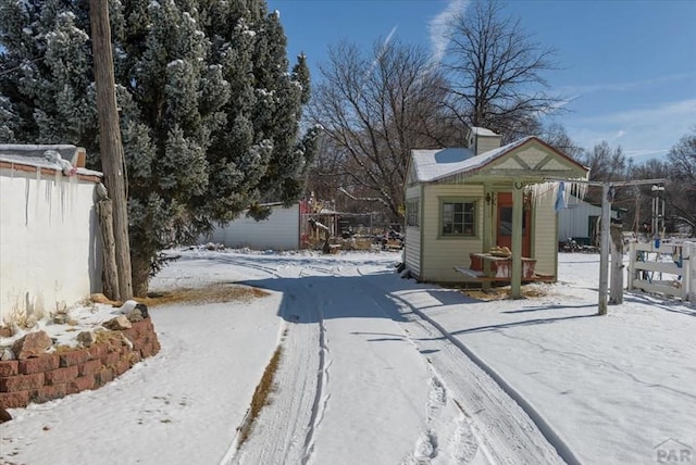 snow covered structure with fence and an outdoor structure