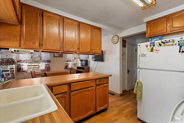 kitchen featuring brown cabinetry, freestanding refrigerator, and light countertops