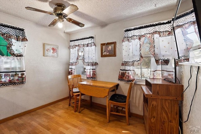 dining space featuring a textured ceiling, baseboards, a ceiling fan, and light wood-style floors