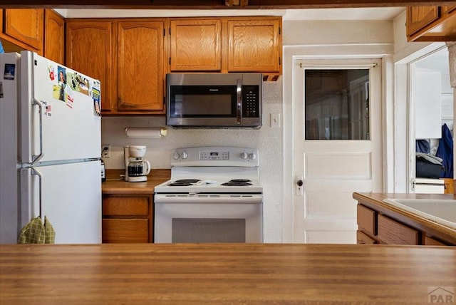 kitchen with brown cabinetry, white appliances, and butcher block countertops