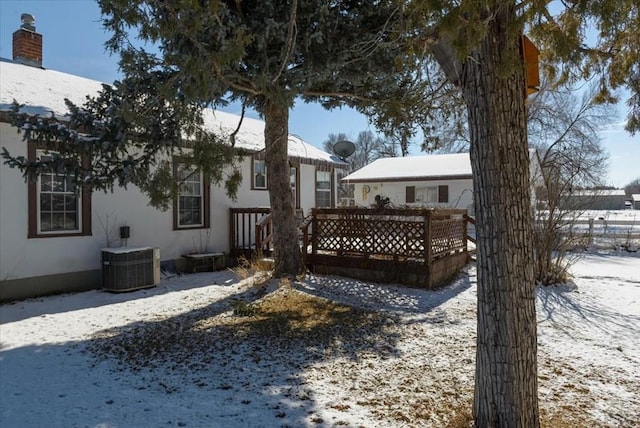 snow covered back of property featuring stucco siding and central air condition unit