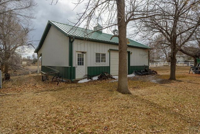 view of side of property featuring metal roof, a chimney, board and batten siding, and fence