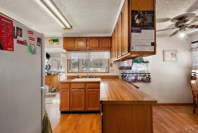 kitchen featuring brown cabinets, light countertops, a textured ceiling, and freestanding refrigerator