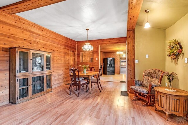 dining area with light wood-type flooring, visible vents, beamed ceiling, and wooden walls