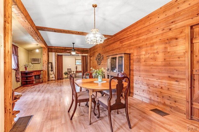 dining space featuring wooden walls, visible vents, beamed ceiling, and light wood-style flooring