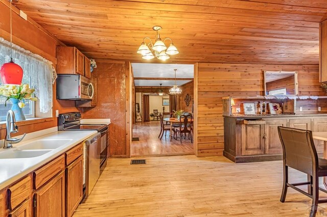 kitchen featuring brown cabinets, a notable chandelier, decorative light fixtures, stainless steel microwave, and a sink