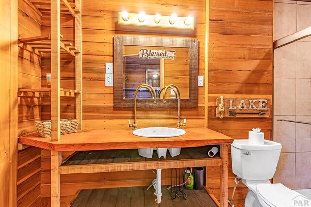 half bath featuring toilet, wooden walls, and a sink