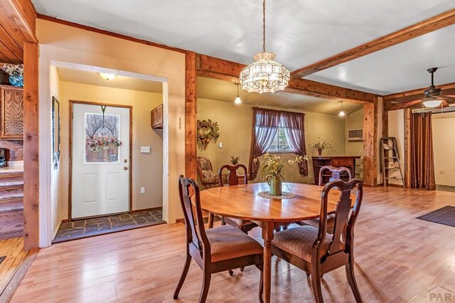 dining area with beam ceiling, a wall mounted air conditioner, and light wood finished floors