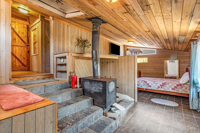 bedroom with lofted ceiling, wood ceiling, a wood stove, and wooden walls