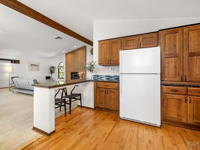 kitchen with vaulted ceiling with beams, a peninsula, open floor plan, freestanding refrigerator, and brown cabinetry