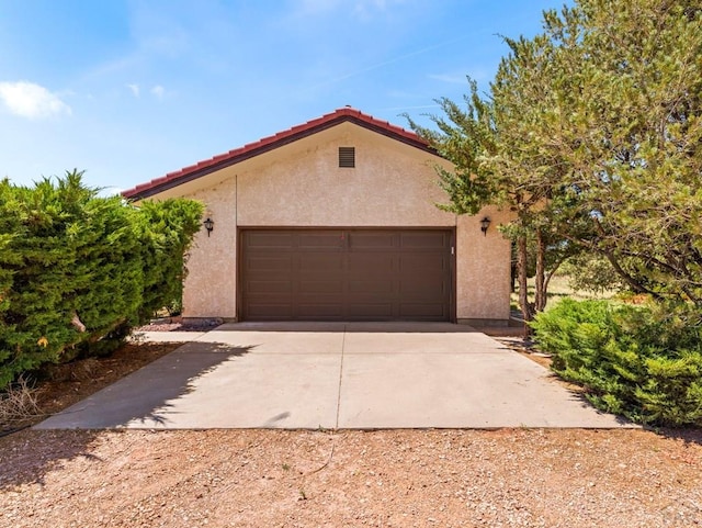 exterior space with a garage, concrete driveway, a tiled roof, an outdoor structure, and stucco siding