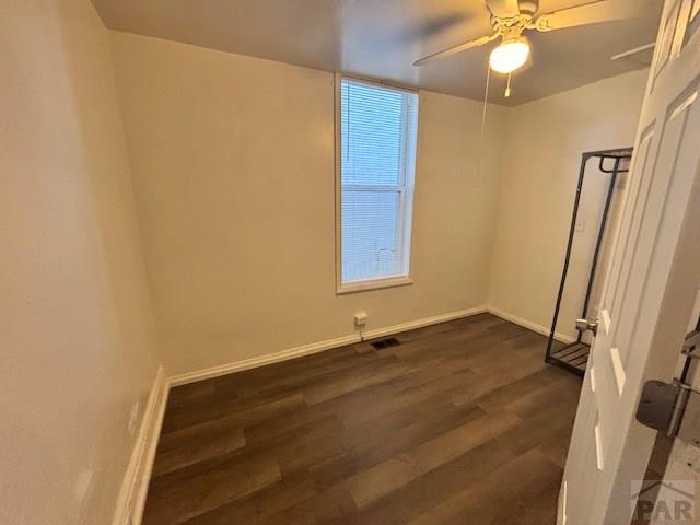 unfurnished room with a ceiling fan, visible vents, baseboards, and dark wood-type flooring