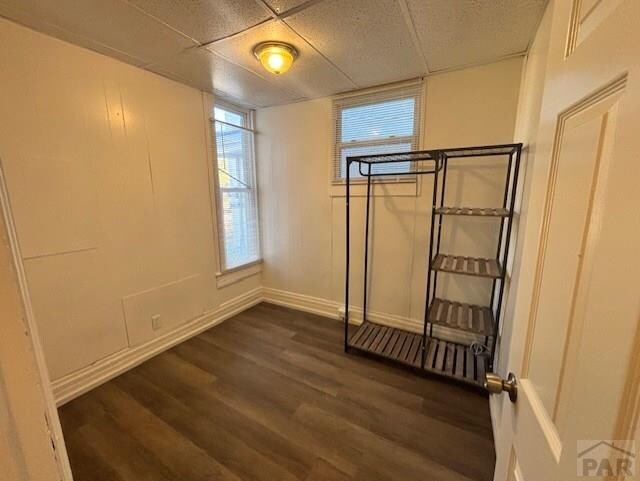 interior space featuring dark wood finished floors, a paneled ceiling, and baseboards