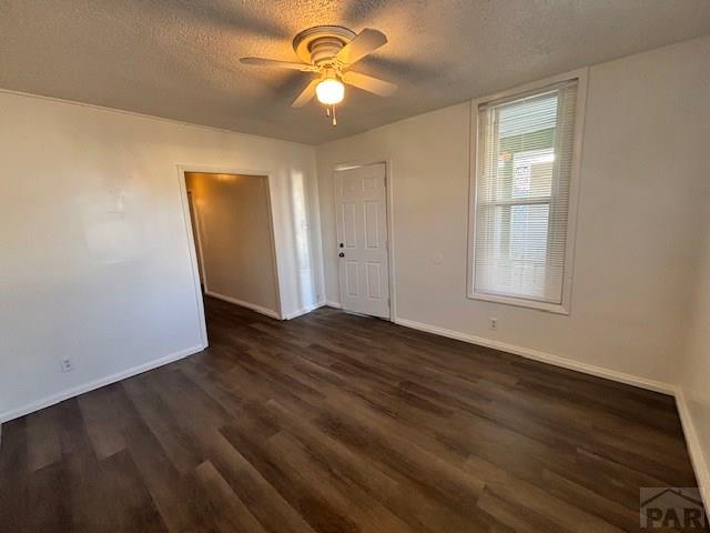 empty room with ceiling fan, a textured ceiling, baseboards, and dark wood-style flooring