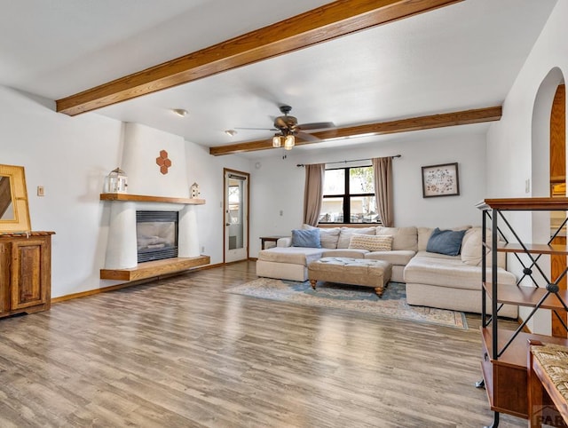 living room featuring a glass covered fireplace, beam ceiling, baseboards, and wood finished floors