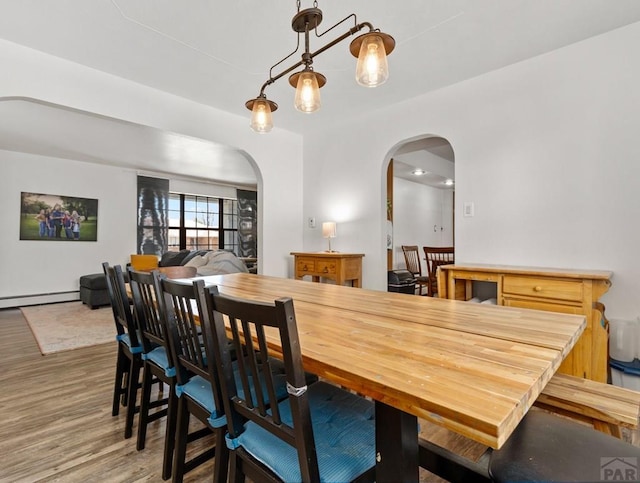 dining area with arched walkways, baseboard heating, and wood finished floors