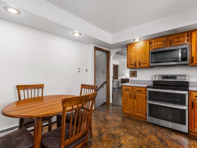 kitchen with arched walkways, appliances with stainless steel finishes, brown cabinets, light countertops, and recessed lighting