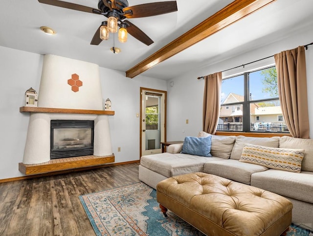 living area with dark wood-style floors, beam ceiling, a glass covered fireplace, ceiling fan, and baseboards