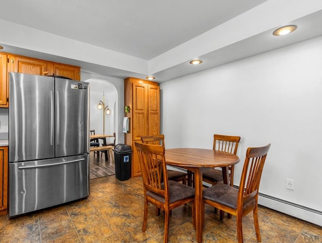 dining area with arched walkways, stone finish floor, a baseboard radiator, and recessed lighting