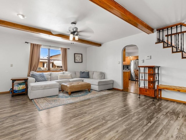 living room featuring arched walkways, beamed ceiling, baseboards, and wood finished floors