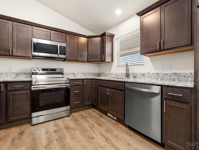 kitchen with light stone counters, stainless steel appliances, lofted ceiling, light wood-style flooring, and dark brown cabinets