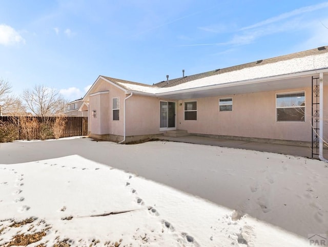 snow covered property with fence and stucco siding