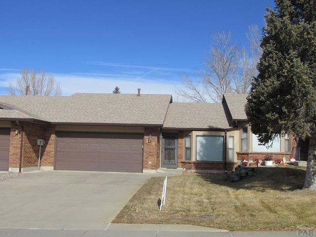 ranch-style home featuring a garage, concrete driveway, roof with shingles, a front lawn, and brick siding