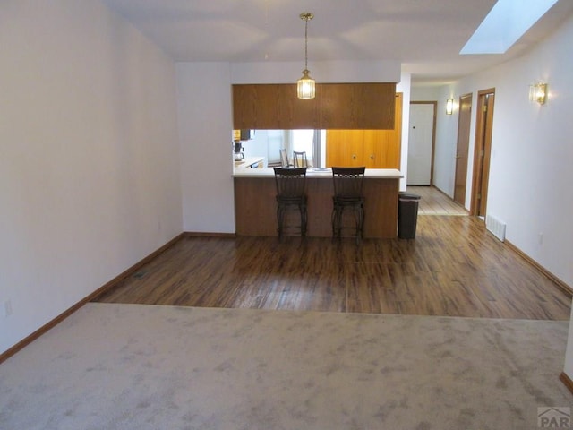 kitchen with a skylight, brown cabinets, dark colored carpet, light countertops, and visible vents