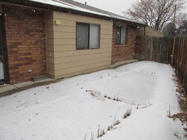 view of snow covered exterior with brick siding and fence