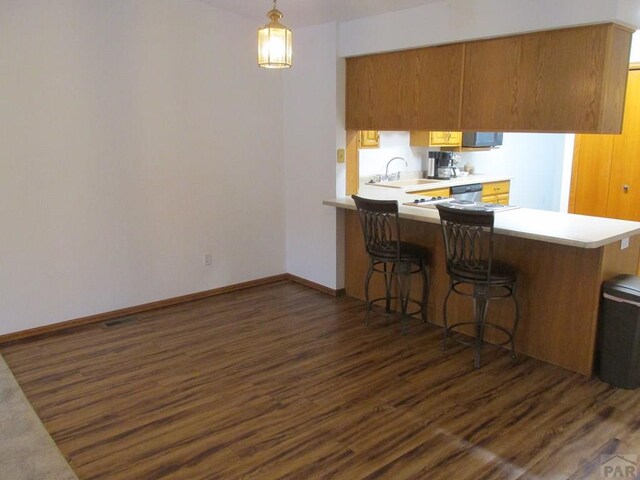 kitchen featuring dark wood-style floors, a kitchen breakfast bar, a peninsula, light countertops, and a sink