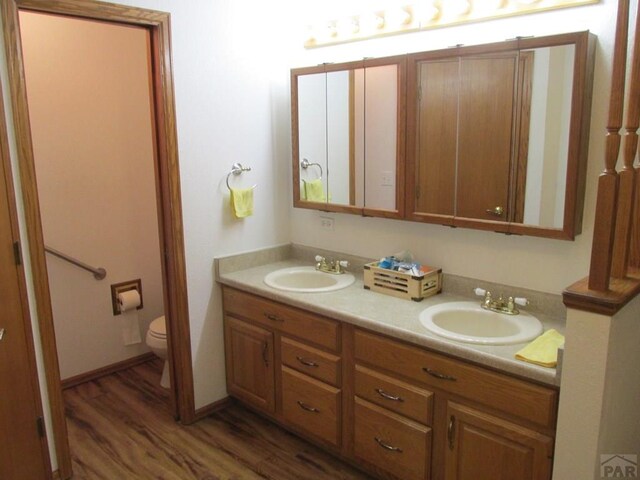 full bath featuring toilet, double vanity, a sink, and wood finished floors