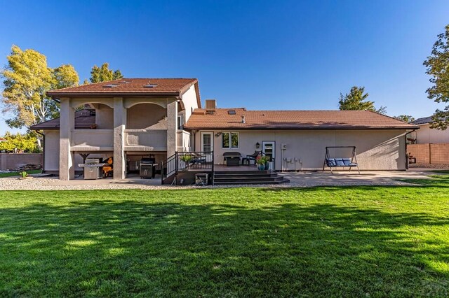 rear view of house featuring a deck, a lawn, a patio area, and stucco siding