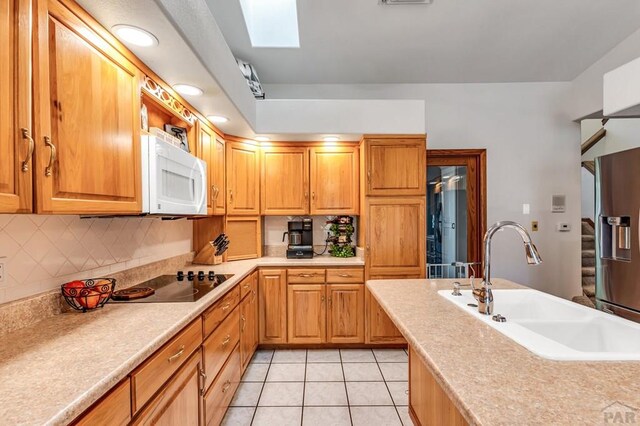 kitchen with a skylight, stainless steel fridge, white microwave, light countertops, and a sink