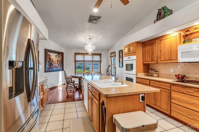 kitchen with light countertops, white appliances, a sink, and a kitchen island with sink