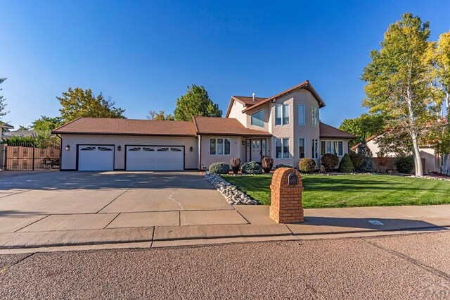 traditional home with stucco siding, a front yard, fence, a garage, and driveway