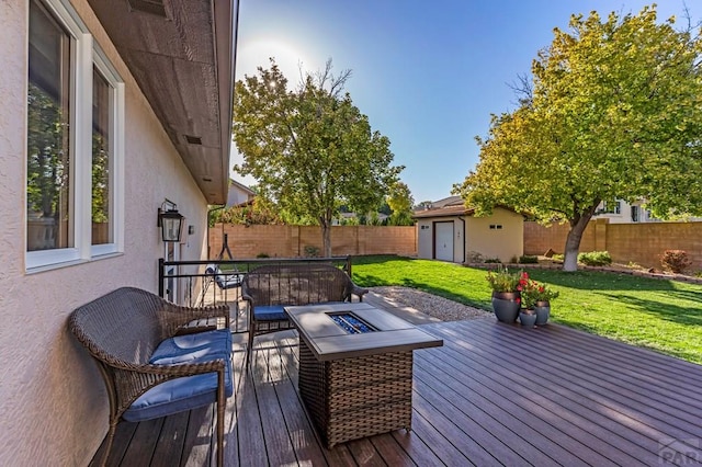 deck with an outbuilding, a fenced backyard, a lawn, and a fire pit