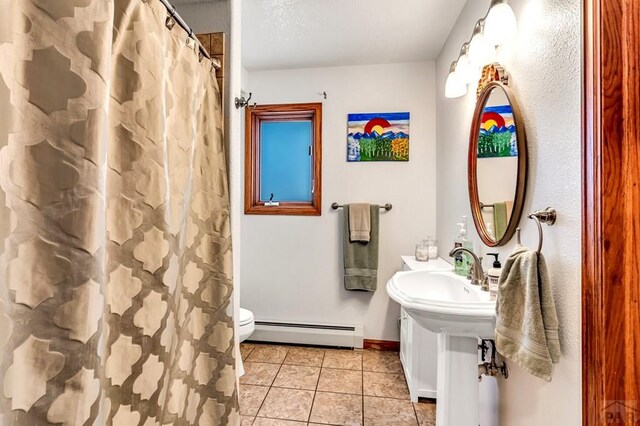 full bath with toilet, a baseboard heating unit, a sink, baseboards, and tile patterned floors