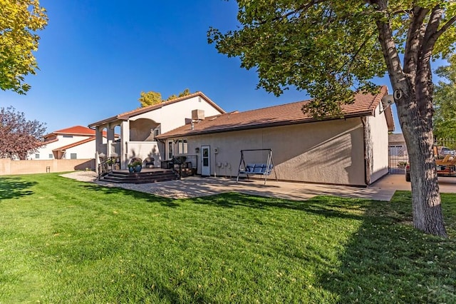 rear view of house featuring stucco siding, fence, a lawn, and a patio