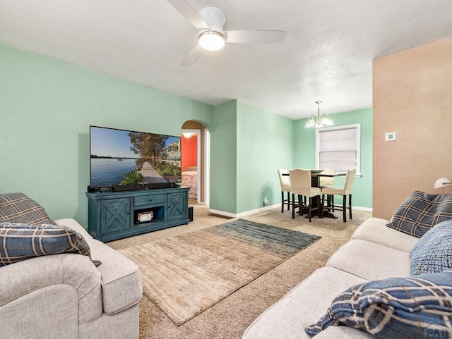 living area with baseboards, ceiling fan, arched walkways, and light colored carpet