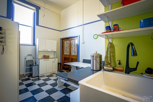 kitchen with open shelves, dark floors, freestanding refrigerator, white cabinetry, and a sink