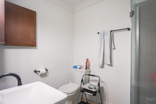 bathroom featuring a shower with door, a sink, toilet, and ornamental molding