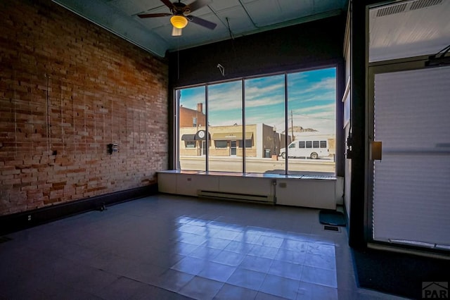 unfurnished room with a baseboard heating unit, ceiling fan, and brick wall