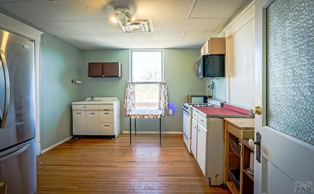 kitchen featuring visible vents, gas range gas stove, hardwood / wood-style floors, freestanding refrigerator, and black microwave