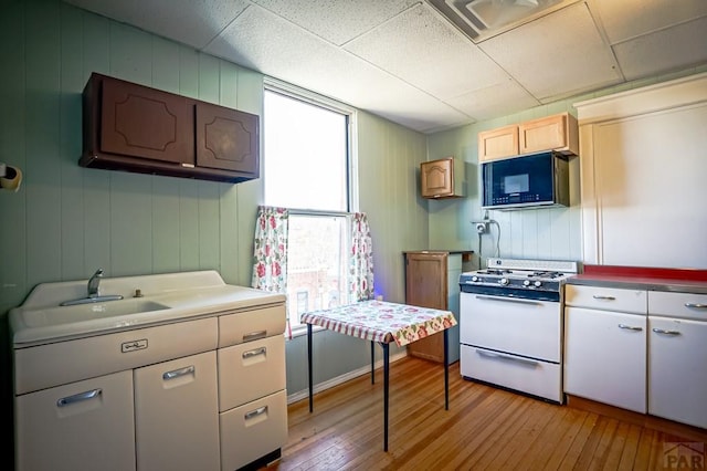 kitchen with gas range gas stove, black microwave, light wood-style floors, a paneled ceiling, and a sink