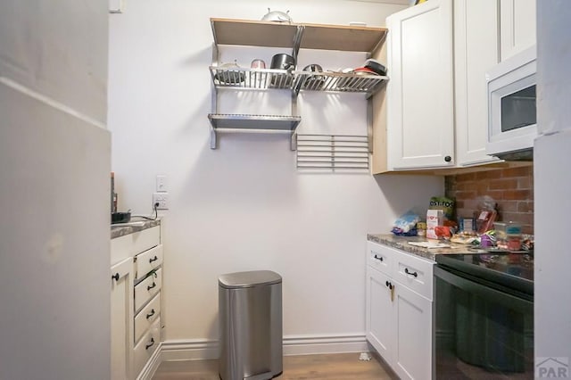 kitchen featuring white microwave, backsplash, baseboards, stove, and white cabinets