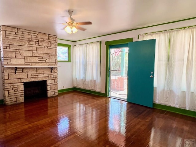 unfurnished living room with a stone fireplace, wood finished floors, a ceiling fan, and baseboards