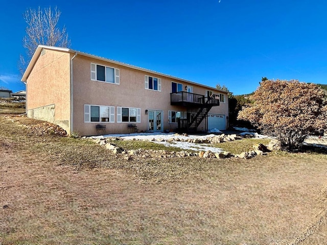 rear view of house with a garage, stairway, and stucco siding