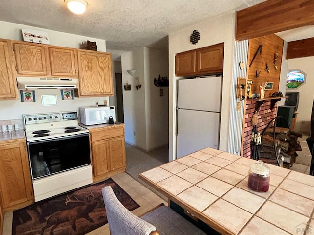 kitchen featuring tile countertops, a brick fireplace, a textured ceiling, white appliances, and under cabinet range hood