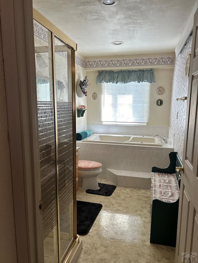 full bathroom featuring a garden tub, a shower stall, toilet, and a textured ceiling
