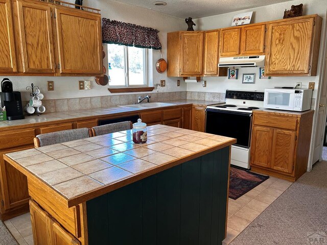 kitchen featuring under cabinet range hood, white appliances, a sink, tile counters, and brown cabinetry